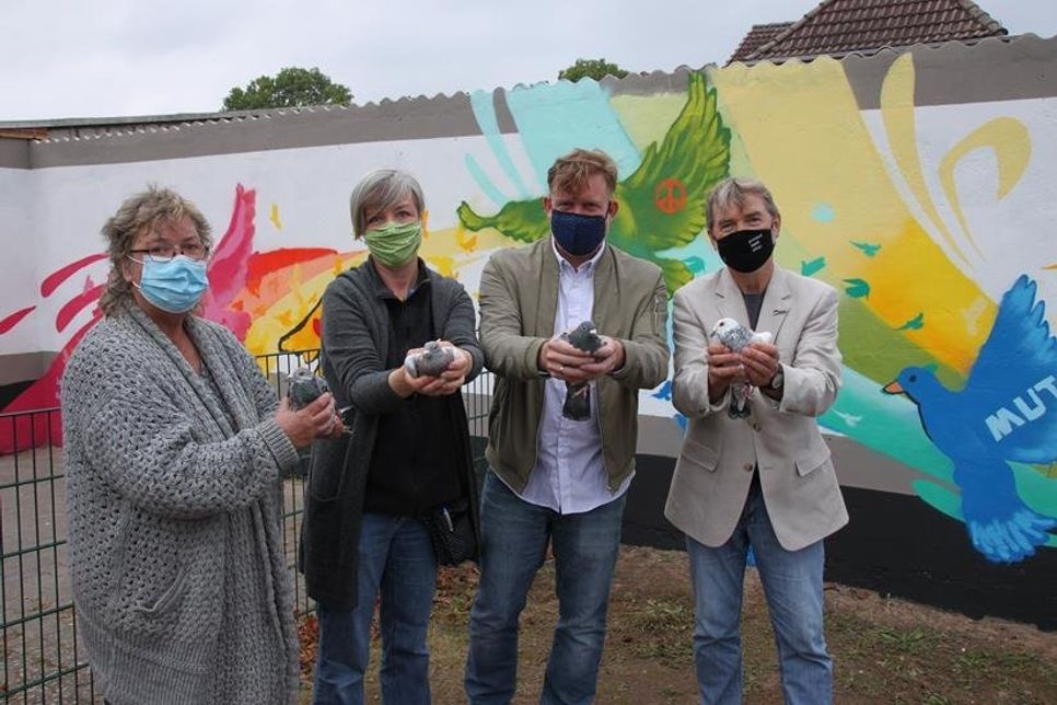 Familie Kuchel stellte die Wand zur Verfügung, die an das Schulgelände angrenzt und sorgte dafür, dass zur Einweihungsfeier echte Friedenstauben in die Lüfte steigen konnten.  Unterstützerin Heike Rhein, Künstler Jan-Malte Strijek alias „Honsar“ und Schulleiter Hans-Peter Hopp (v. lks.) freuten sich über dieses starke Symbol.