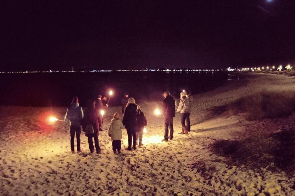 Warm eingemummelte Strandbesucher versammeln sich um den Holsteiner Wander-Guide und entzünden mit ihm gemeinsam ihre Fackeln.