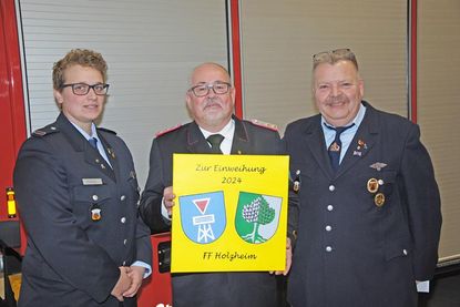 Michael Wilkat (m.) freut sich über das Geschenk der Partnerfeuerwehr aus Holzheim (Rheinland-Pfalz), das deren Wehrführer Dirk Weber und Stellvertreterin Sarah Kolter mitgebracht hatten: „…wird einen ehrenvollen Platz erhalten“.