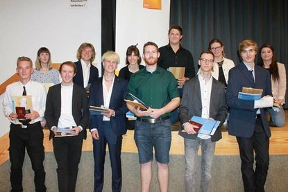 12 Auszubildende des Tischlerhandwerks halten stolz ihren Gesellenbrief in der Hand.