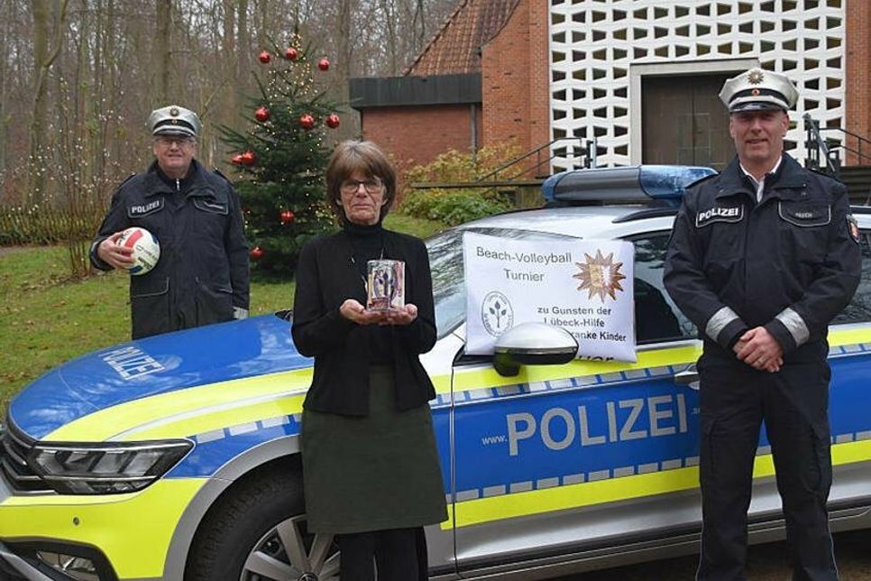 Spendenübergabe der Polizeidirektion Lübeck vor der Waldkirche in Timmendorfer Strand: Heidi Menorca, Vorsitzende Lübeck-Hilfe für krebskranke Kinder e.V., freut sich über die Spende, die Organisator Nicky Päsch (rechts) und Stationsleiter Jörg Wischnewski (hinten) stellvertretend für alle Polizeibeamten und Sponsoren überreicht haben.