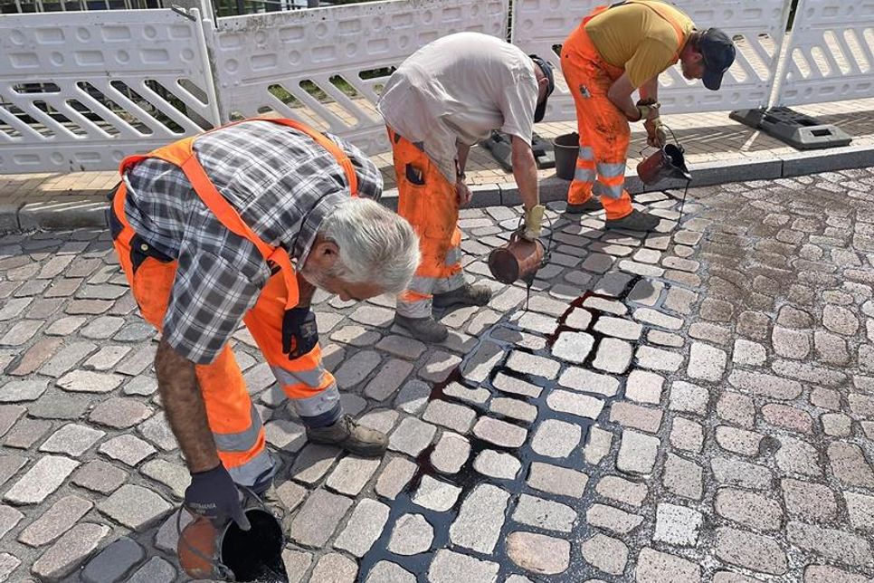 Straßenbauer gießen eine schwarze, klebrige Flüssigkeit in die Fugen zwischen den Pflastersteinen.