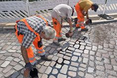 Straßenbauer gießen eine schwarze, klebrige Flüssigkeit in die Fugen zwischen den Pflastersteinen.