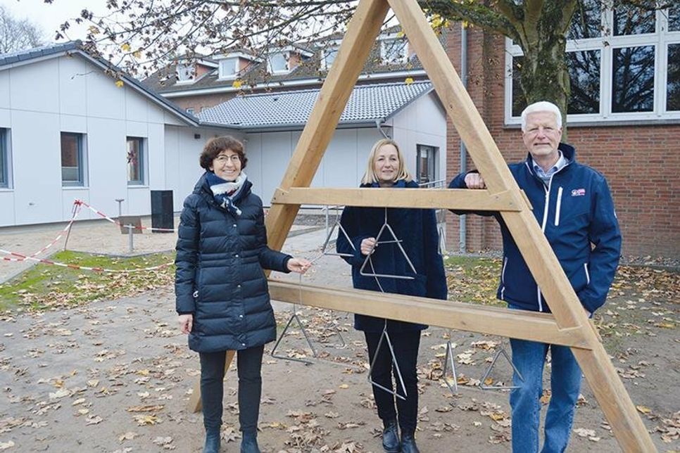 Elisabeth Steinhoff (l.), Schulleiterin Förderzentrum „Schule am Papenmoor“, Susanne Voß, Vorstand der Lebenshilfe Ostholstein e.V. und Andreas Gurth aus dem Vorstand der Friedrich Bluhme und Else Jebsen-Stiftung testen die Triangel (im Hintergrund vor den neuen Holzhütten ist die Klangsäule zu sehen).