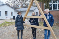 Elisabeth Steinhoff (l.), Schulleiterin Förderzentrum „Schule am Papenmoor“, Susanne Voß, Vorstand der Lebenshilfe Ostholstein e.V. und Andreas Gurth aus dem Vorstand der Friedrich Bluhme und Else Jebsen-Stiftung testen die Triangel (im Hintergrund vor den neuen Holzhütten ist die Klangsäule zu sehen).