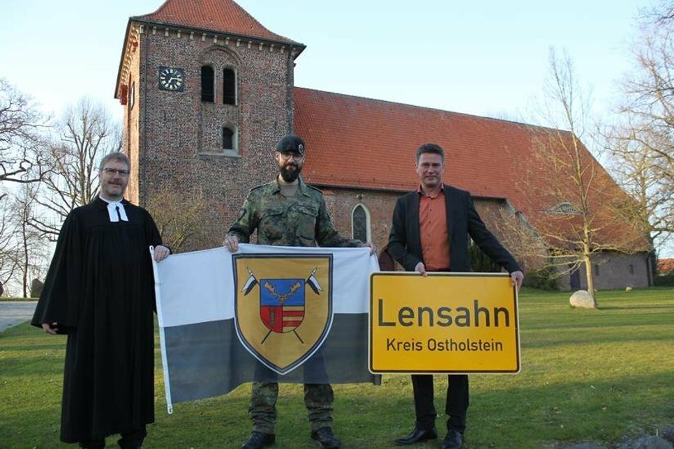 Das Ortsschild der Gemeinde Lensahn geht mit in den Kosovo, während die Kompaniefahne in der Zeit des Einsatzes vor dem Lensahner Rathaus weht. Den Tausch vollzogen Pastor Jörg Reimann, Hauptmann Gideon-Phillip Möller und Bürgermeister Michael Robien (v. lks.).