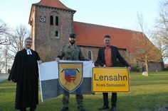 Das Ortsschild der Gemeinde Lensahn geht mit in den Kosovo, während die Kompaniefahne in der Zeit des Einsatzes vor dem Lensahner Rathaus weht. Den Tausch vollzogen Pastor Jörg Reimann, Hauptmann Gideon-Phillip Möller und Bürgermeister Michael Robien (v. lks.).