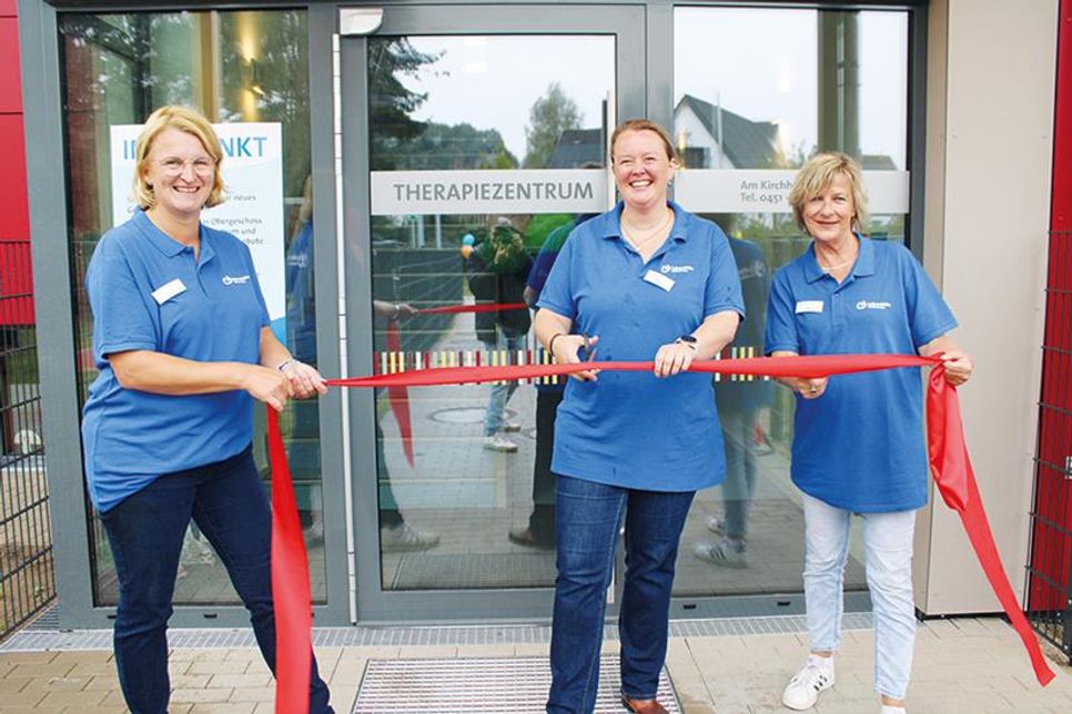 Jessica Groß, Vorstand Lebenshilfe Ostholstein e.V. (Mitte), schneidet mit Hilfe von Kita-Leiterin Melanie Müller (links) und Anke Jeßberger, Leiterin des Therapiezentrums, für den „reporter“ das rote Band durch.