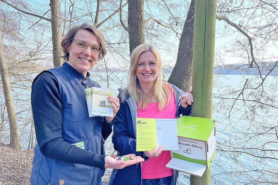 Stephanie Fahnemann vom Naturpark Holsteinische Schweiz und Caroline Backmann, Tourismuszentrale Holsteinische Schweiz, präsentierten einen der neuen Stempelkästen am Schöhsee-Wanderweg in Plön.