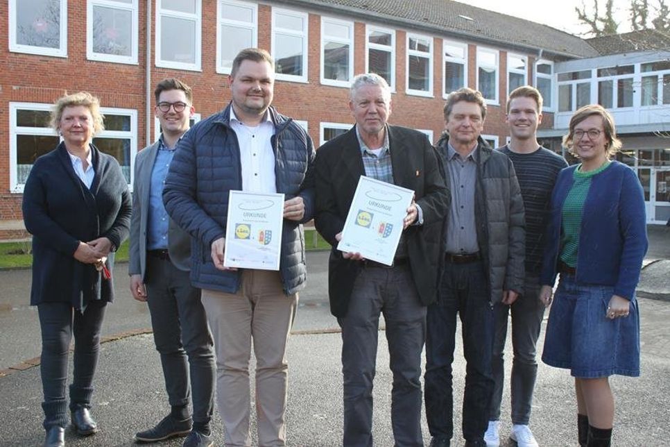 Die Vertreter von Schule, Lidl und der Partnerschaft Schule-Betrieb mit Urkunde auf dem Schulhof der Grund- und Gemeinschaftsschule.