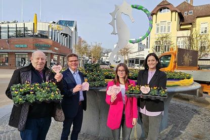 Wolfgang Rahlf vom Blumen- und Pflanzenmarkt Rahlf (von links), Tourismusdirektor Joachim Nitz, TSNT-Azubi Louisa Ernst und Marketingleiterin Silke Szymoniak mit den Herzuntersetzern vor dem Brunnen mit den ersten Frühblühern.