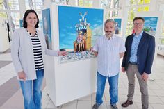 Silke Szymoniak, Marketingleiterin der TSNT GmbH, Cartoonist Frank Bahr (Mitte) und Tourismuschef Joachim Nitz bei der Eröffnung der neuen Ausstellung in der Trinkkurhalle.