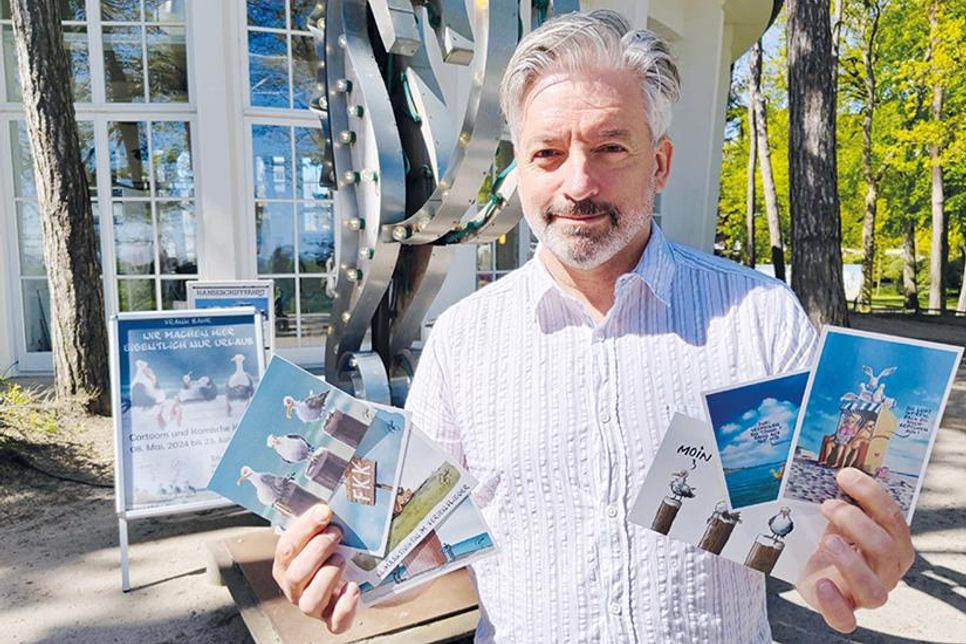 Cartoonist Frank Bahr mit einigen seiner Motiven auf Postkarten vor der Trinkkurhalle in Timmendorfer Strand.