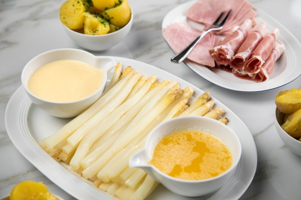 Klassisch serviert: Frischer weißer Spargel mit Sauce Hollandaise, zerlassener Butter, Kartoffeln und Schinken.