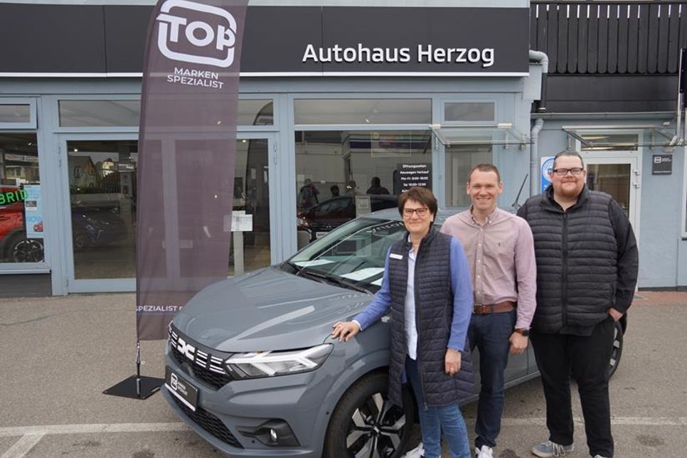 Die Geschäftsführung mir Regina und Dennis Herzog sowie Verkaufsberater Markus Voß (v. lks.) vor einem Dacia-Modell.