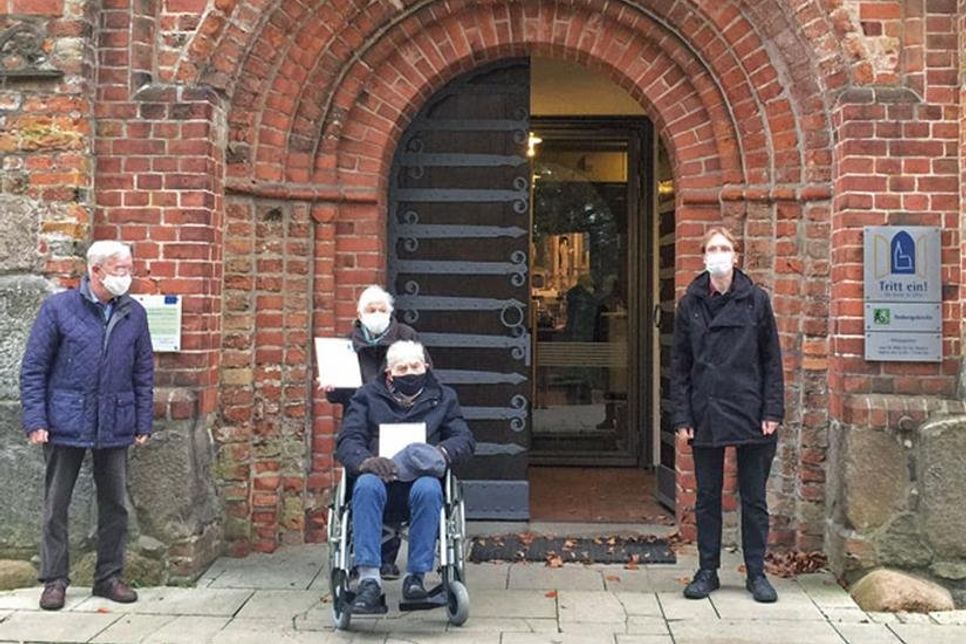 Hütedienstleiter Klaus Kasper (links) und Pastor Andreas Gruben (rechts) überreichen vor dem Kirchenportal der St.-Johannis-Kirche die Dankurkunden an Karin und Hans Peters.