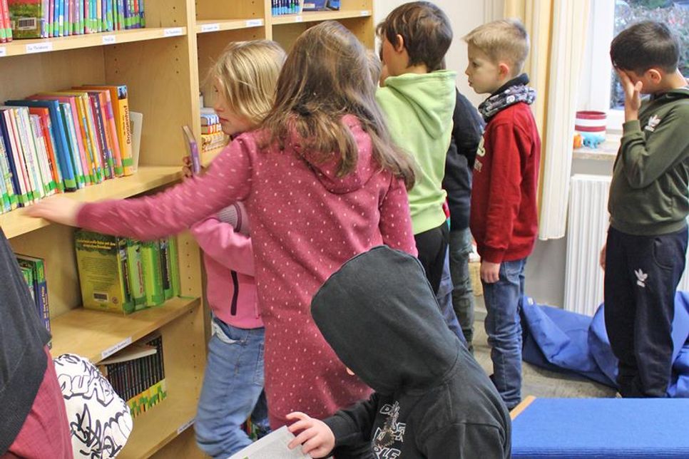 Die Kinder durchstöbern den Bücherbestand in den Regalen der Bücherei.