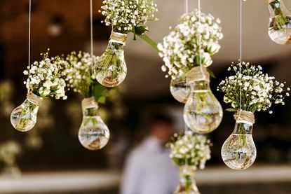 Zarte Blüten in schwebenden Glühbirnenvasen sind eine einfache und stilvolle Dekoidee, die sich perfekt in das florale Gesamtkonzept der Hochzeit einfügt.