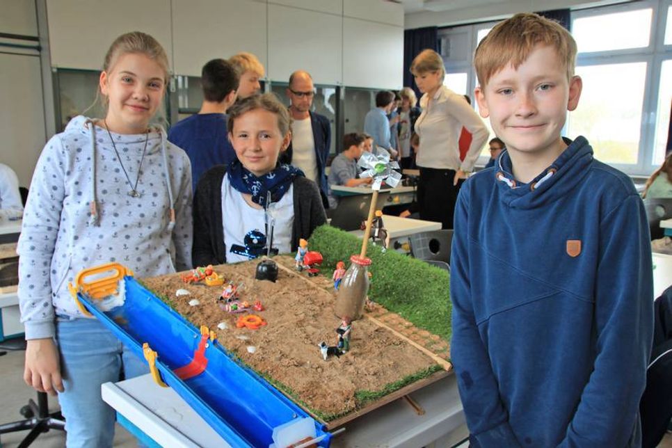 Bei den 5. Klässlern Cay-Eckard, Frida und Lucy (v. re.) bildeten Playmobilfiguren, Kunstrasen, Sand, ein künstlicher Deich und ein Regenrohr die Kulisse für ihre Anlage zur Energiegewinnung durch Wasser und Wind.