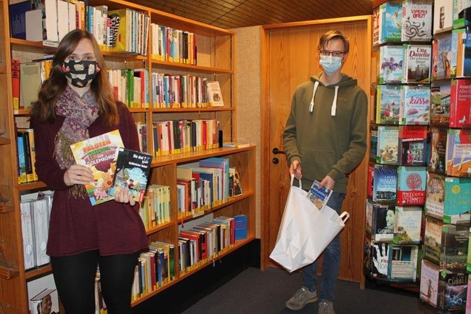 Mitarbeiterin Laura Dorittke und Auszubildender Janek Beckmann bieten eine kontaktlose Übergabe der Bücher an.