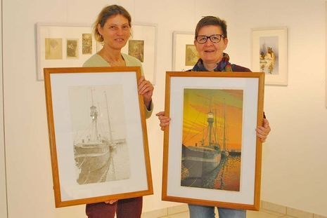 Zwei Kunsttechniken im Vergleich: Während Sabine Behrens (links) eine Zeichnung des „alten Feuerschiffs“ zeigt, hält Sigrid Paulsen- McCord das selbe Motiv als Farbdruck in ihren Händen.