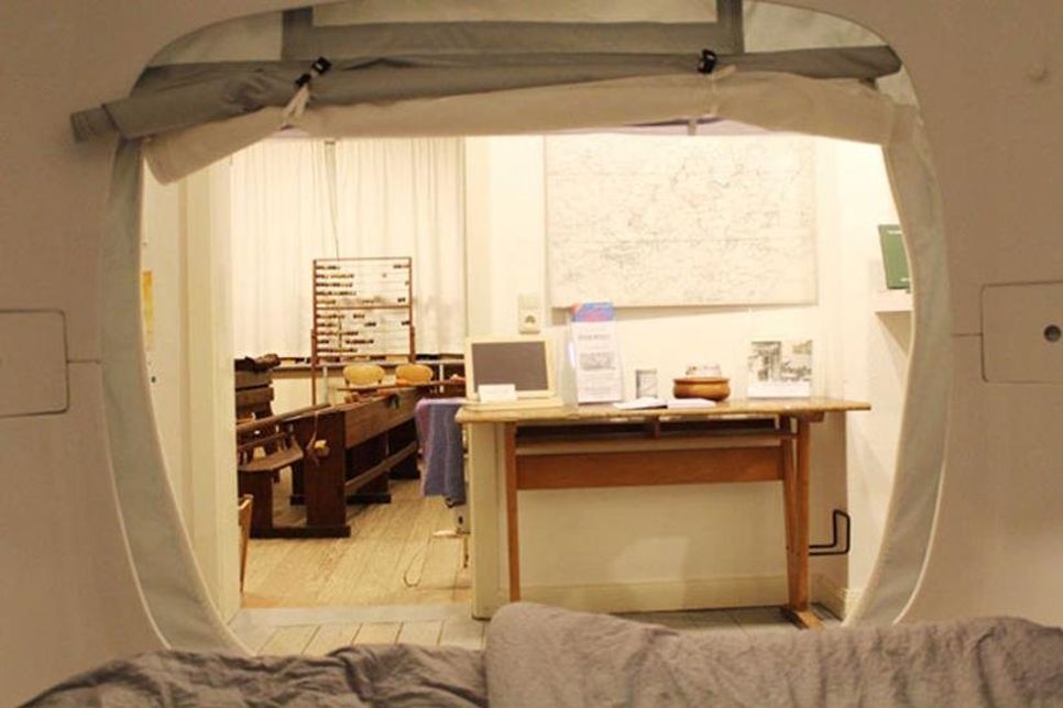 Aus dem gemütlichen „sleep Cube“ schauen die Gäste direkt in das historische Klassenzimmer mit seinen hölzernen Schulbänken, Schiefertafeln und Lehrerpult.
