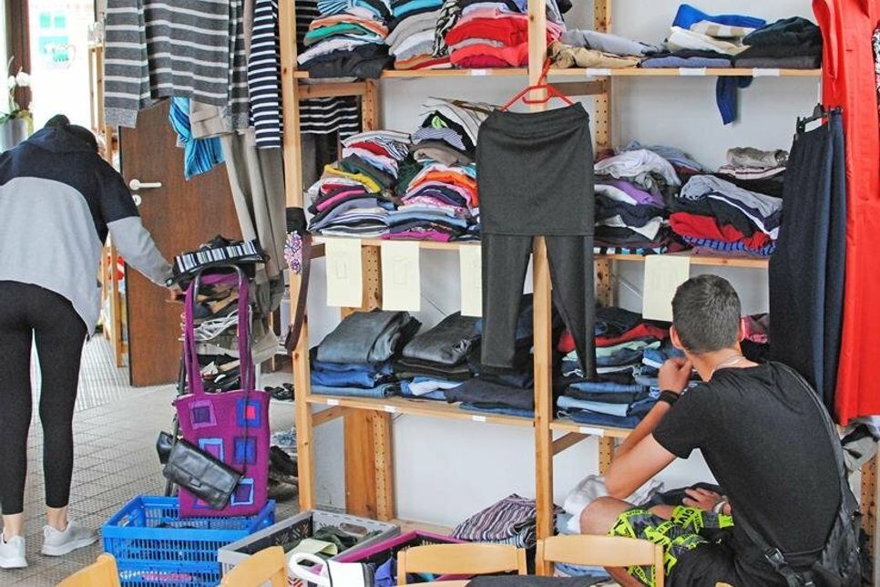 In der AWO Begegnungsstätte für Geflüchtete sucht eine junge Frau nach einem Paar Sandalen, während ein Junge das Kleiderregal nach einer passenden Hose durchstöbert.