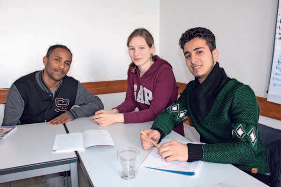 Maru Eshetu aus Eritrea (links) und Kusai Kreem aus Syrien (rechts) lassen sich von Manou Gomlich bei ihren Deutschaufgaben helfen.